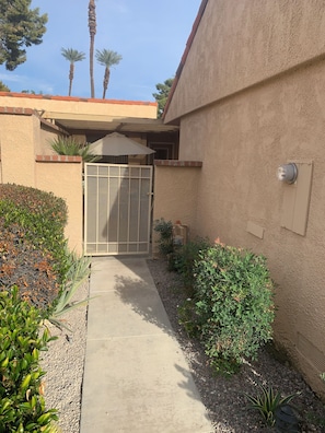 A gated entrance with a concrete pathway leading to a building with stucco walls and a red roof. - Our Little Gem In The Desert (Rancho Mirage)