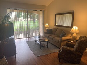 Ein Wohnzimmer mit Sofa, Sessel, Couchtisch, Fernseher und zwei Lampen.