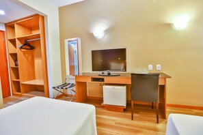 Una habitación de hotel con un escritorio de madera, televisión, refrigerador pequeño, una silla y una cama.