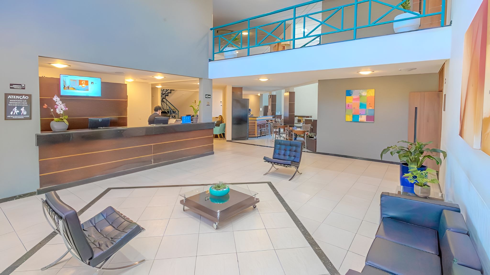 Um hall de hotel moderno com balcão de recepção, área de estar e escadaria para um andar superior.