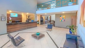 Um hall de hotel moderno com balcão de recepção, área de estar e escadaria para um andar superior.