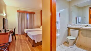 Ein Hotelzimmer mit einem Holztisch, einem Fernseher, zwei Betten, einem Badezimmer mit Toilette und Waschbecken sowie einem großen Spiegel.