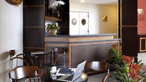 Een modern café met een laptop op een tafel, houten stoelen, een koelkast en een kamerplant.