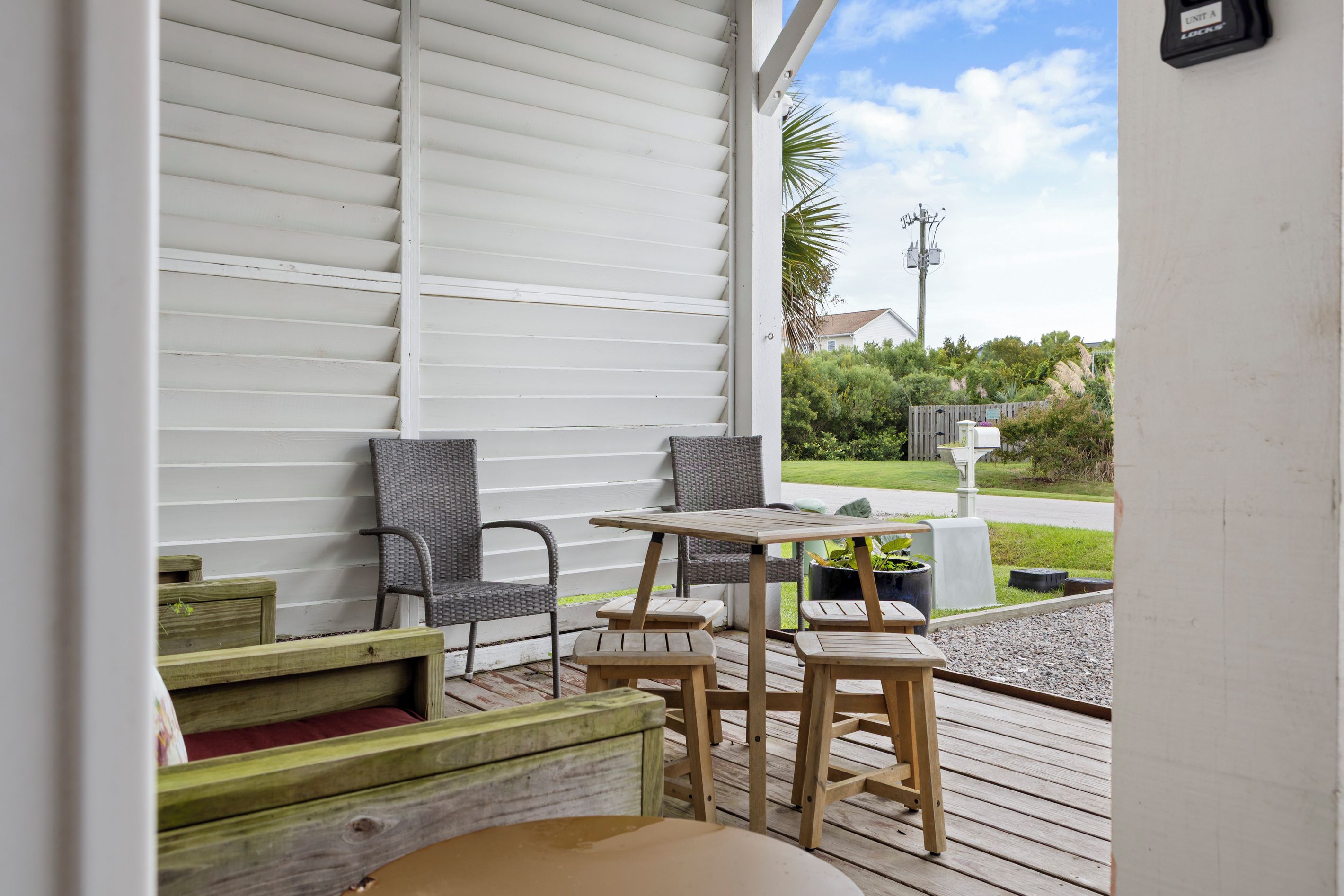 A covered outdoor seating area with a table and chairs, a wooden bench, and a view of a residential street.