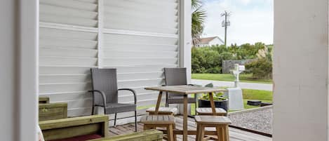 A covered outdoor seating area with a table and chairs, a wooden bench, and a view of a residential street.