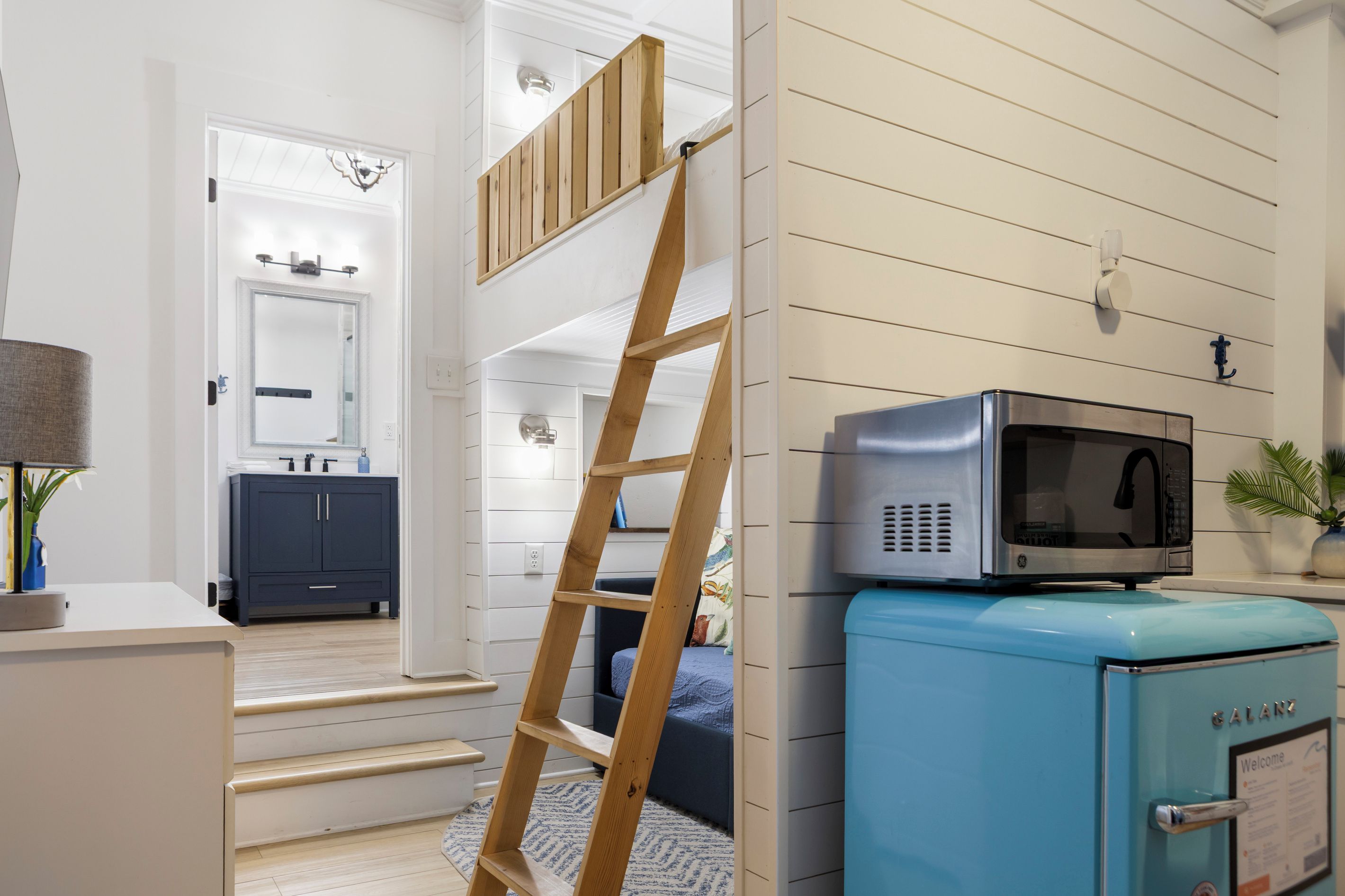 Eine moderne Küche mit einer Mikrowelle auf einem blauen Gerät, Holzstufen, die zu einer Tür führen, und eine an der Wand angelehnte Leiter.