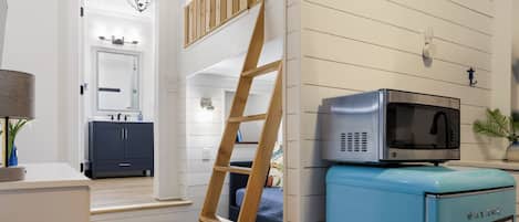 Eine moderne Küche mit einer Mikrowelle auf einem blauen Gerät, Holzstufen, die zu einer Tür führen, und eine an der Wand angelehnte Leiter.