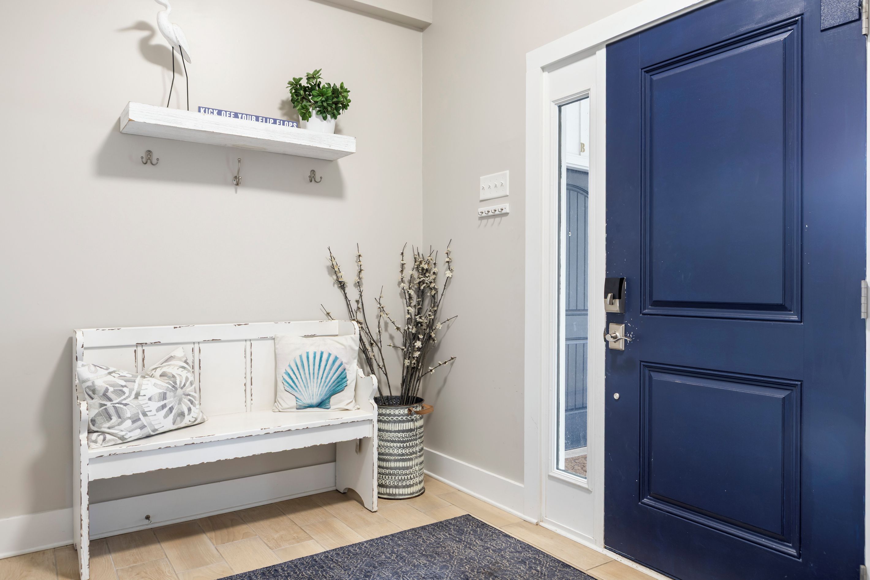 A room with a white bench, a blue door, a white wall, and a small potted plant.