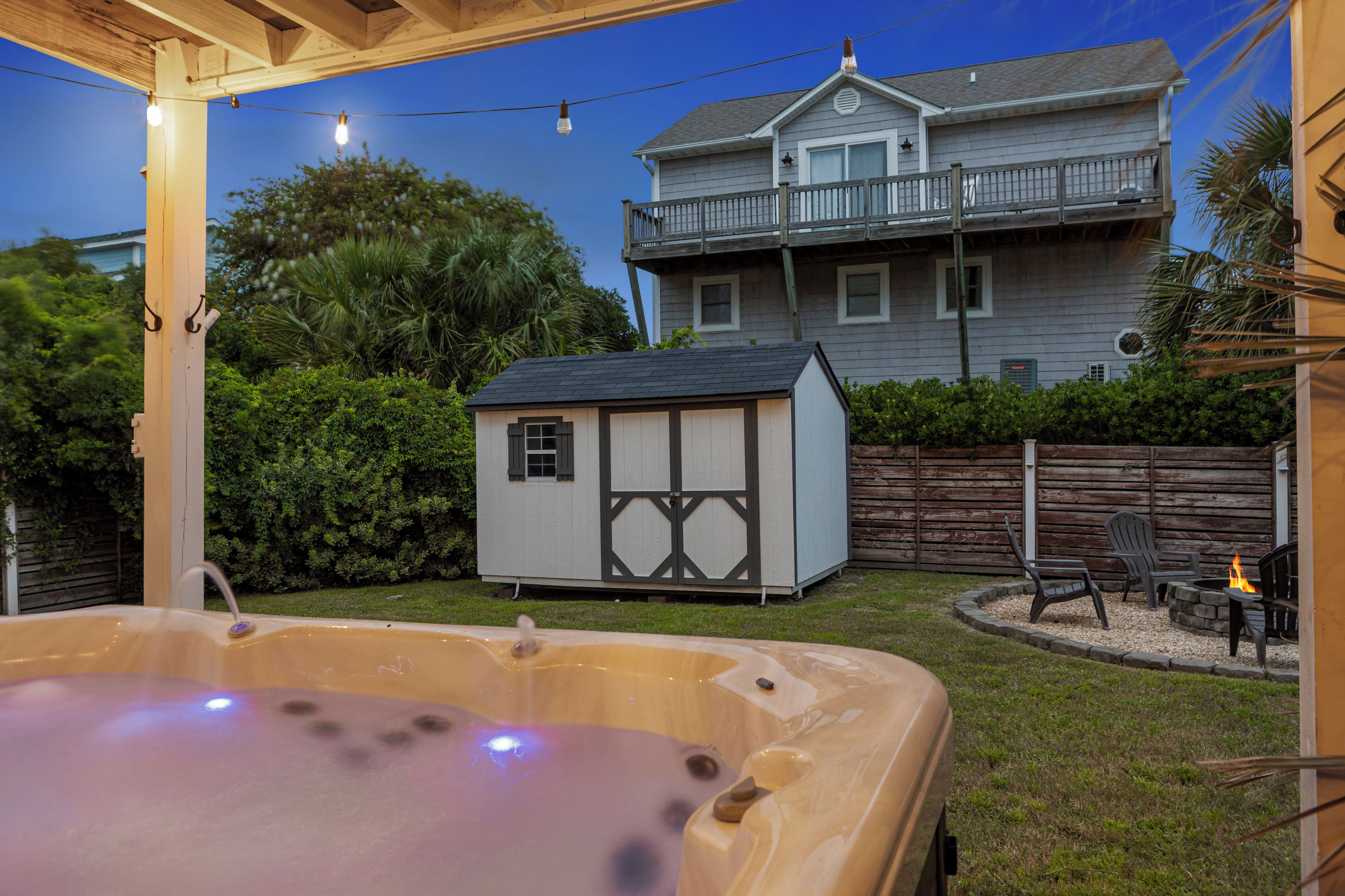 Ein Garten mit Whirlpool, einer kleinen Gartenhütte und einer Terrasse mit Stühlen und einem Feuerkorb.