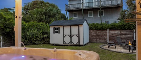 A backyard with a hot tub, a small shed, and a patio area with chairs and a fire pit.
