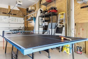 Un tavolo da ping pong in una stanza con un portone da garage, scaffali con diversi oggetti e un sacchetto di Kingfisher Match Light.