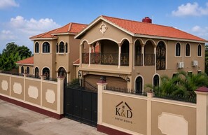 Un edificio de dos pisos con fachada color beige, techo de tejas rojas y entrada protegida por una reja.