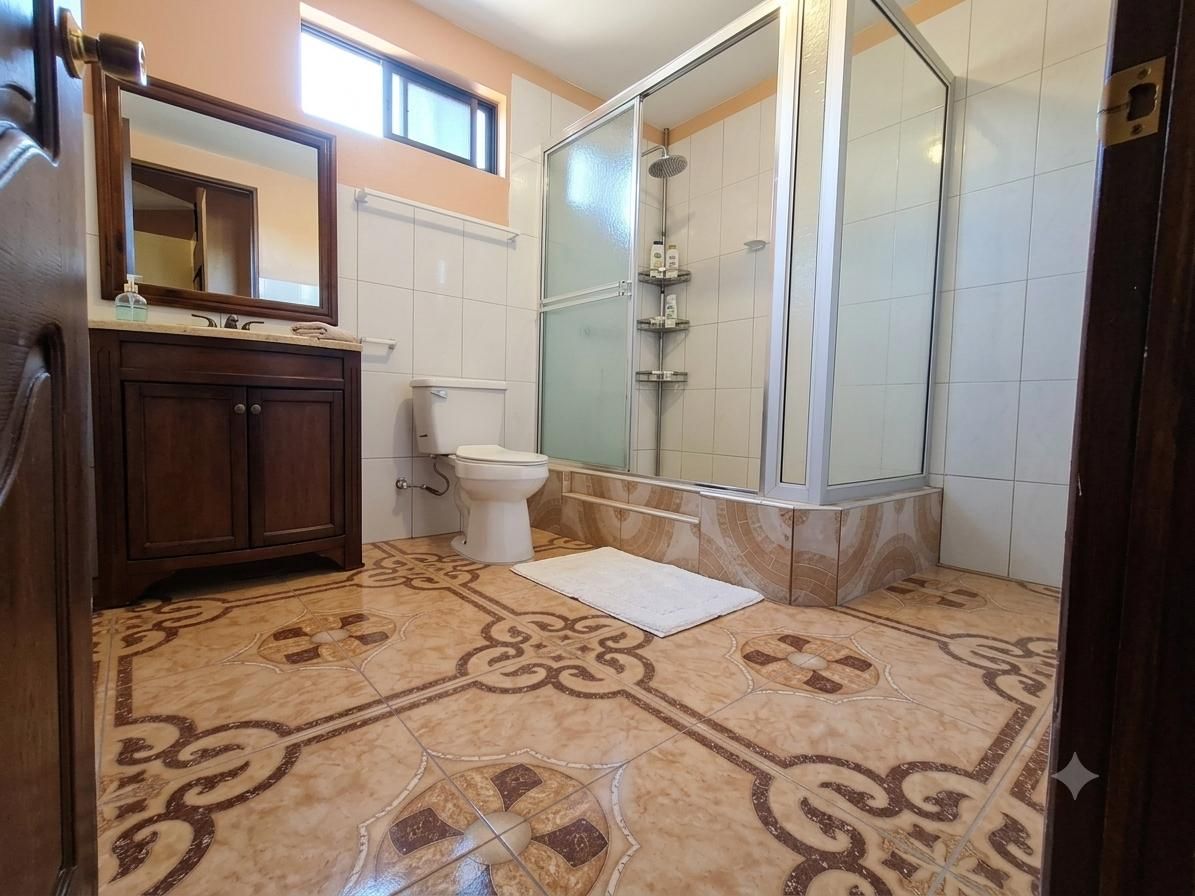 Une salle de bain équipée d’une douche, de toilettes, d’un lavabo et de carreaux de sol à motifs.