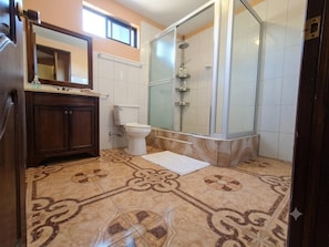 Un baño con ducha, inodoro, tocador y baldosas de suelo estampadas.