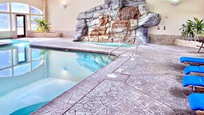 An indoor swimming pool with a rock wall, clear pool water, and blue lounge chairs.