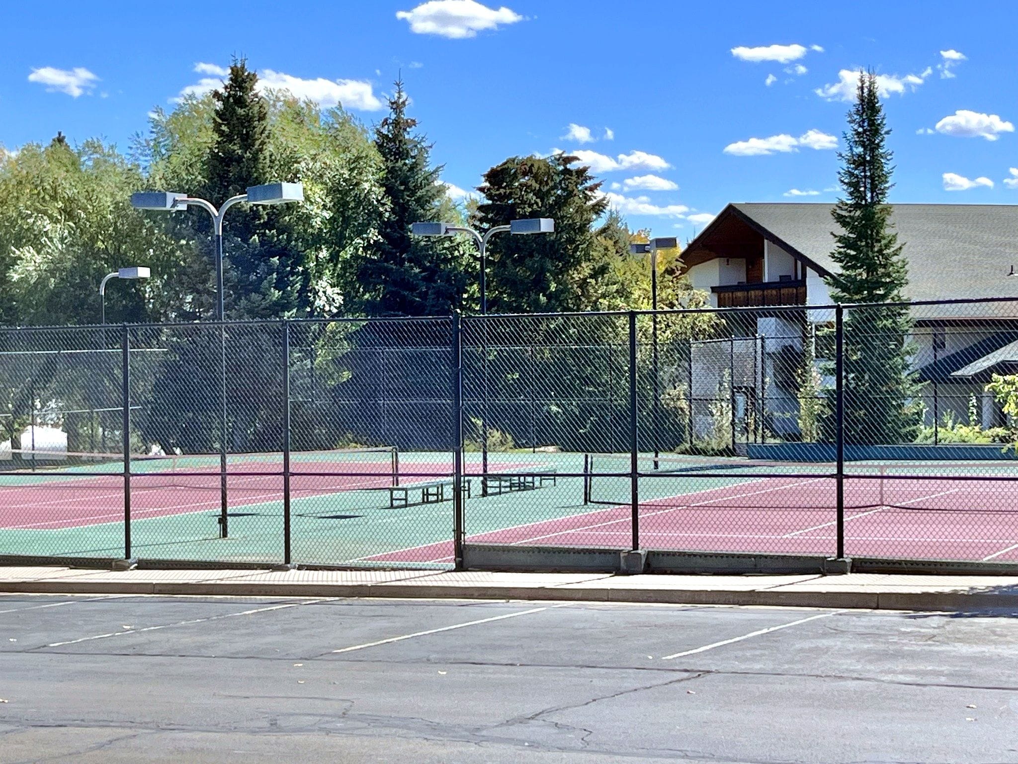 Ein durch einen Zaun umgebener Tennisplatz mit einem Gebäude im Hintergrund.