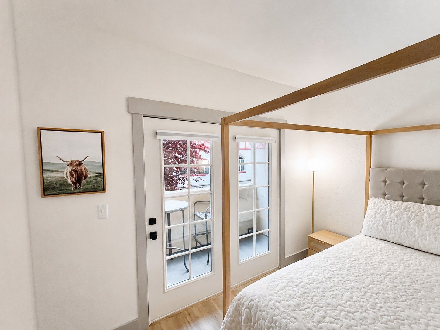 Un dormitorio con cama, una mesita de noche, una lámpara y una puerta que da a un balcón con una silla.