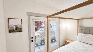 A bedroom with a bed, a bedside table, a lamp, and a door leading to a balcony with a chair.