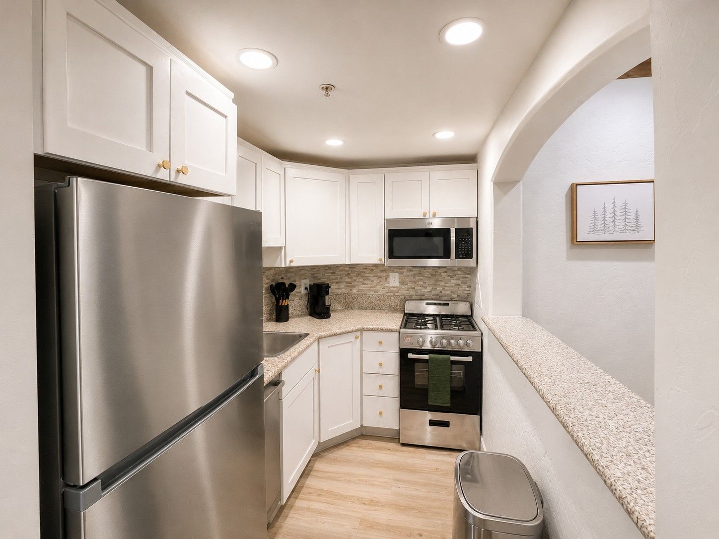 A compact kitchen with white cabinets, stainless steel appliances, and a tiled backsplash.