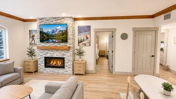 A modern living room with a fireplace, a sofa, a dining table, and a hallway leading to a bedroom.