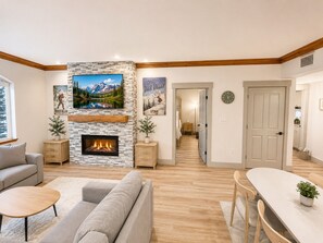 Una sala moderna con chimenea, un sofá, una mesa de comedor y un pasillo que conduce a un dormitorio.