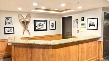 Un espace d’accueil doté d’un comptoir en bois, de photographies encadrées accrochées au mur et d’un plafond pourvu d’un éclairage encastré.