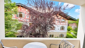 A balcony with a table and two chairs, overlooking a building with a red and white facade and a tree with purple leaves.