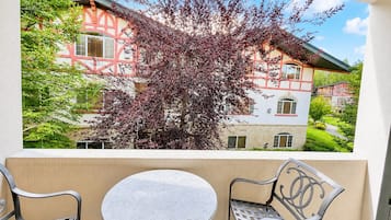 Un balcon avec une table et deux chaises, donnant sur un immeuble à la façade rouge et blanche et sur un arbre aux feuilles violettes.