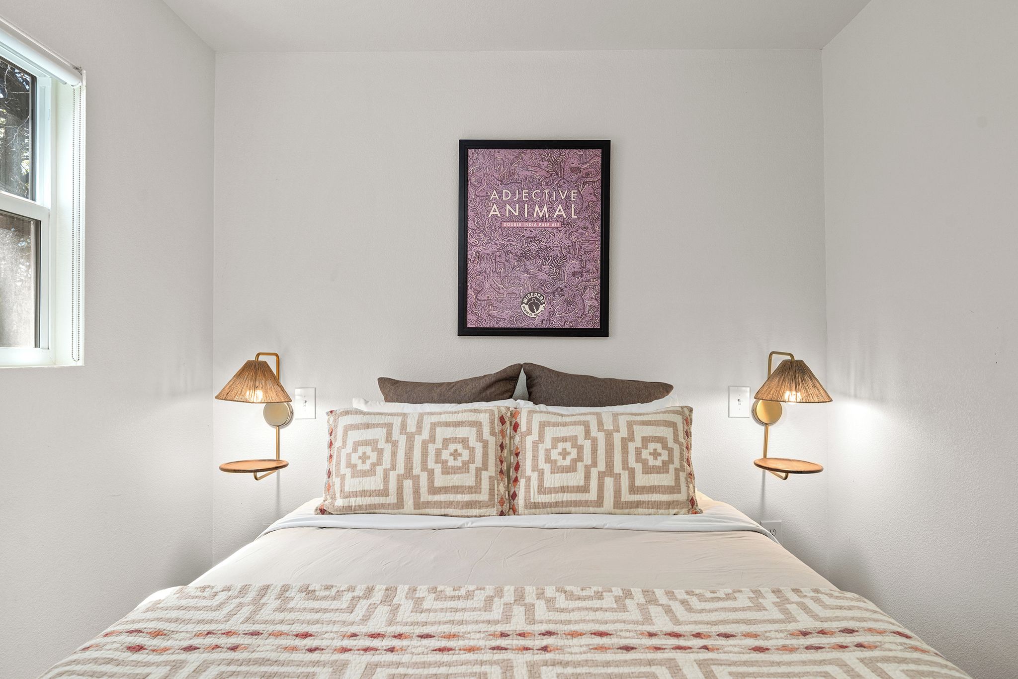 A bedroom with a bed, patterned pillows, a framed picture on the wall, and bedside lamps.