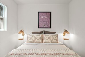 A bedroom with a bed, patterned pillows, a framed picture on the wall, and bedside lamps.