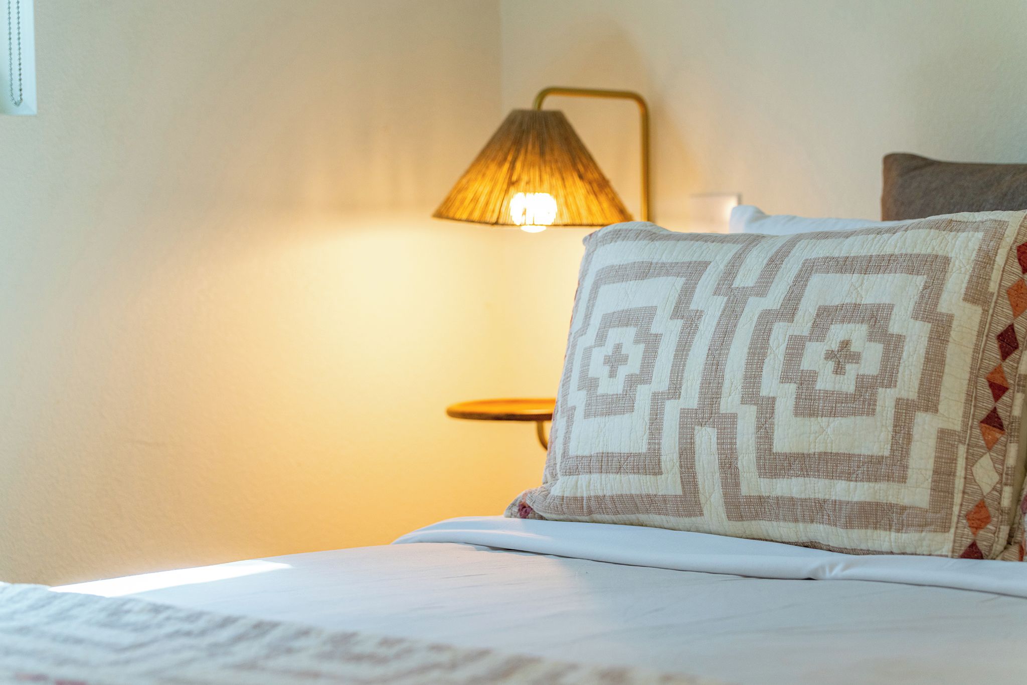 A bed with a patterned pillow and a lamp in the background.