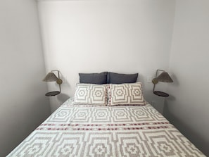 Un lit avec une literie à motifs, deux oreillers et deux lampes fixées au mur.