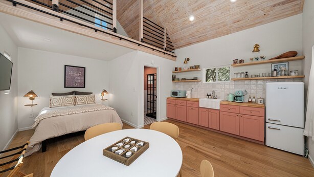 Una cocina moderna con gabinetes rosados, un refrigerador blanco y una zona de comedor con una mesa redonda.