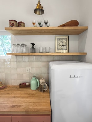 Une cuisine avec un réfrigérateur blanc, un plan de travail en bois, une machine à café et une étagère contenant des bocaux en verre et un tableau encadré.