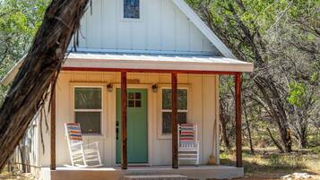 A small, single-story building with a green door and two rocking chairs outside.