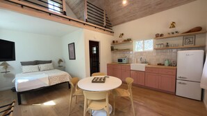 Een kleine hotelkamer met een bed, nachtkastje en een kitchenette.