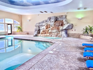 Una piscina interna con parete rocciosa, acqua cristallina e confortevoli poltrone da relax blu.