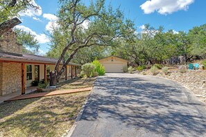A residential property with a garage, a stone building, and a driveway leading to a house. - Gathering Oak | Cozy Fire Pit & Fall Getaway (Wimberly)