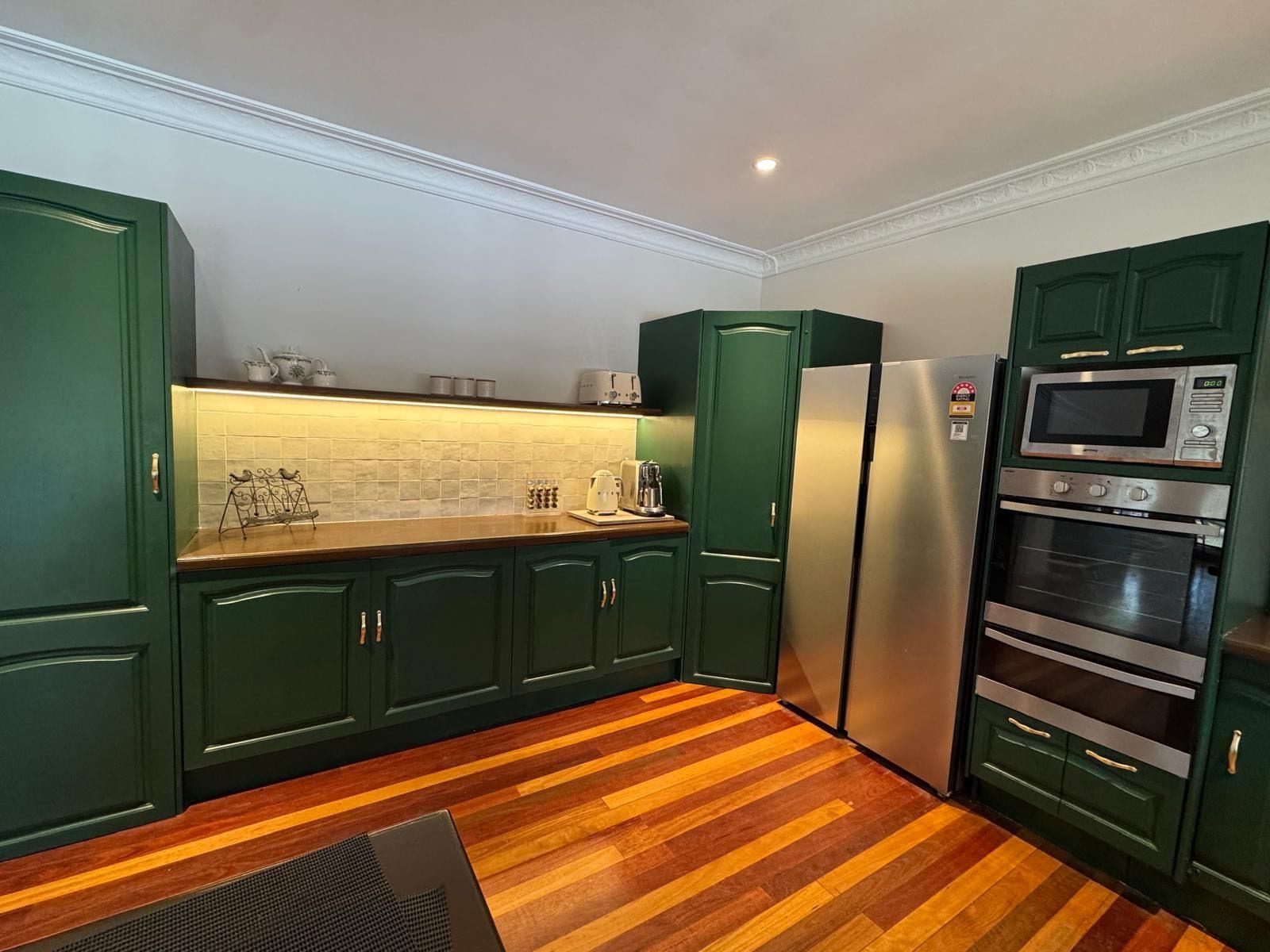 Eine Küche mit grünen Schränken, einem Edelstahl-Kühlschrank, einer Mikrowelle und einem Backofen.