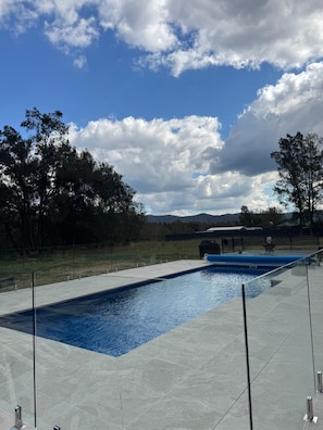 Ein rechteckiger Pool mit klar blauem Wasser, umgeben von einer gepflasterten Liegefläche.