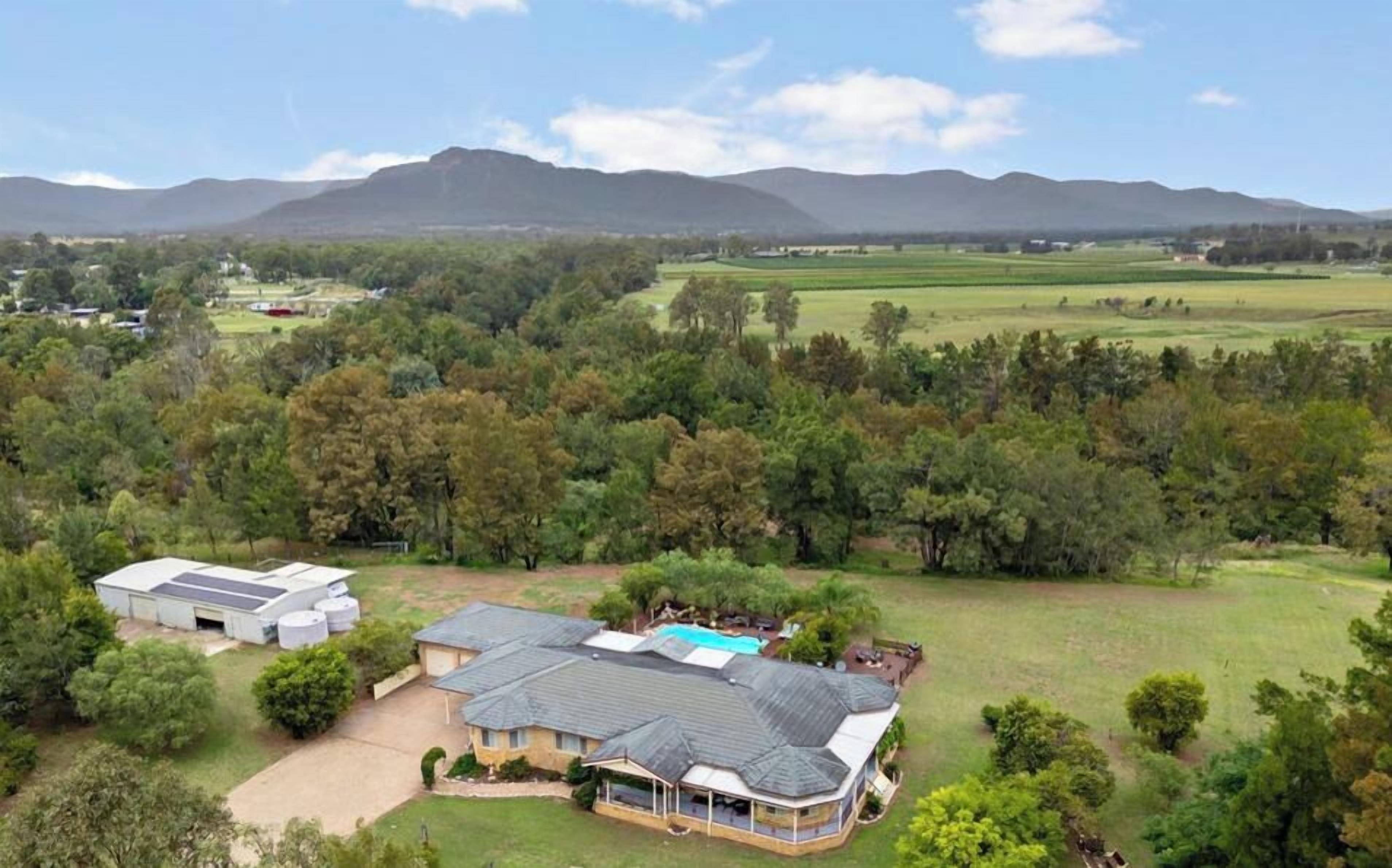 A residential property with a large house, a swimming pool, and a surrounding landscape with trees and distant mountains.