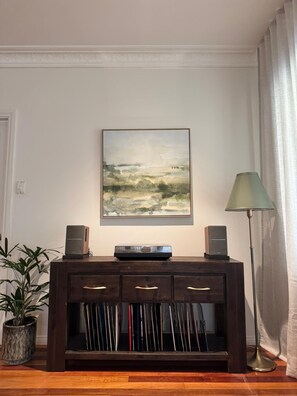 Ein Zimmer mit einer dunklen Holztruhe, einem gerahmten abstrakten Gemälde, einer Stehlampe und einer Topfpflanze.