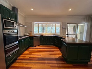 A kitchen with a wooden herringbone floor, dark green cabinetry, and a large window providing natural light. - Harrowby Country House. New Magnesium Pool. Outdoor firepit. Sleeps 11. (Broke)