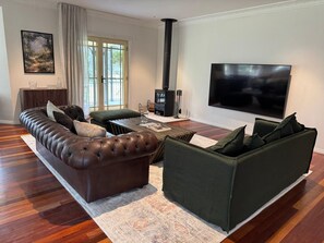 Ein Wohnzimmer mit einer Ledersofa, einem grünen Sofa, einem Kamin und einem großen Fernseher.