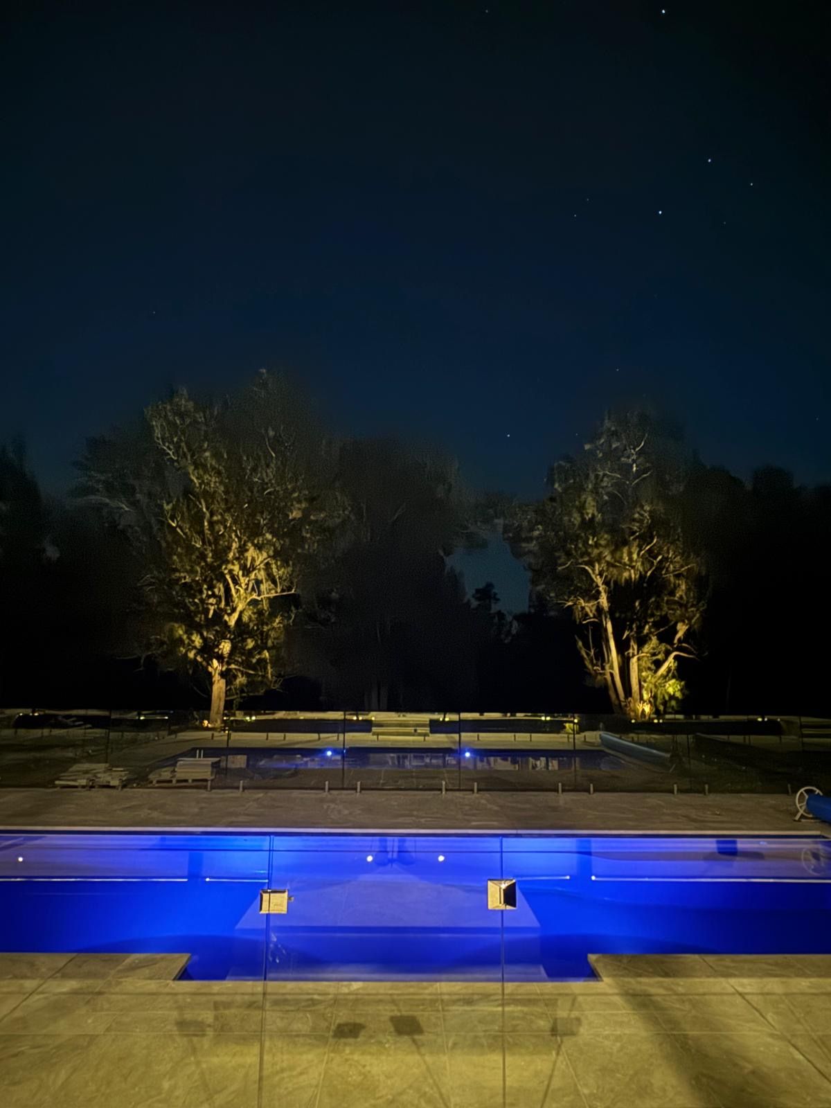 An outdoor swimming pool area at night with trees and a clear sky.