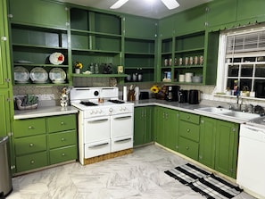 Une cuisine avec des meubles de couleur verte, une cuisinière blanche et un dosseret carrelé.