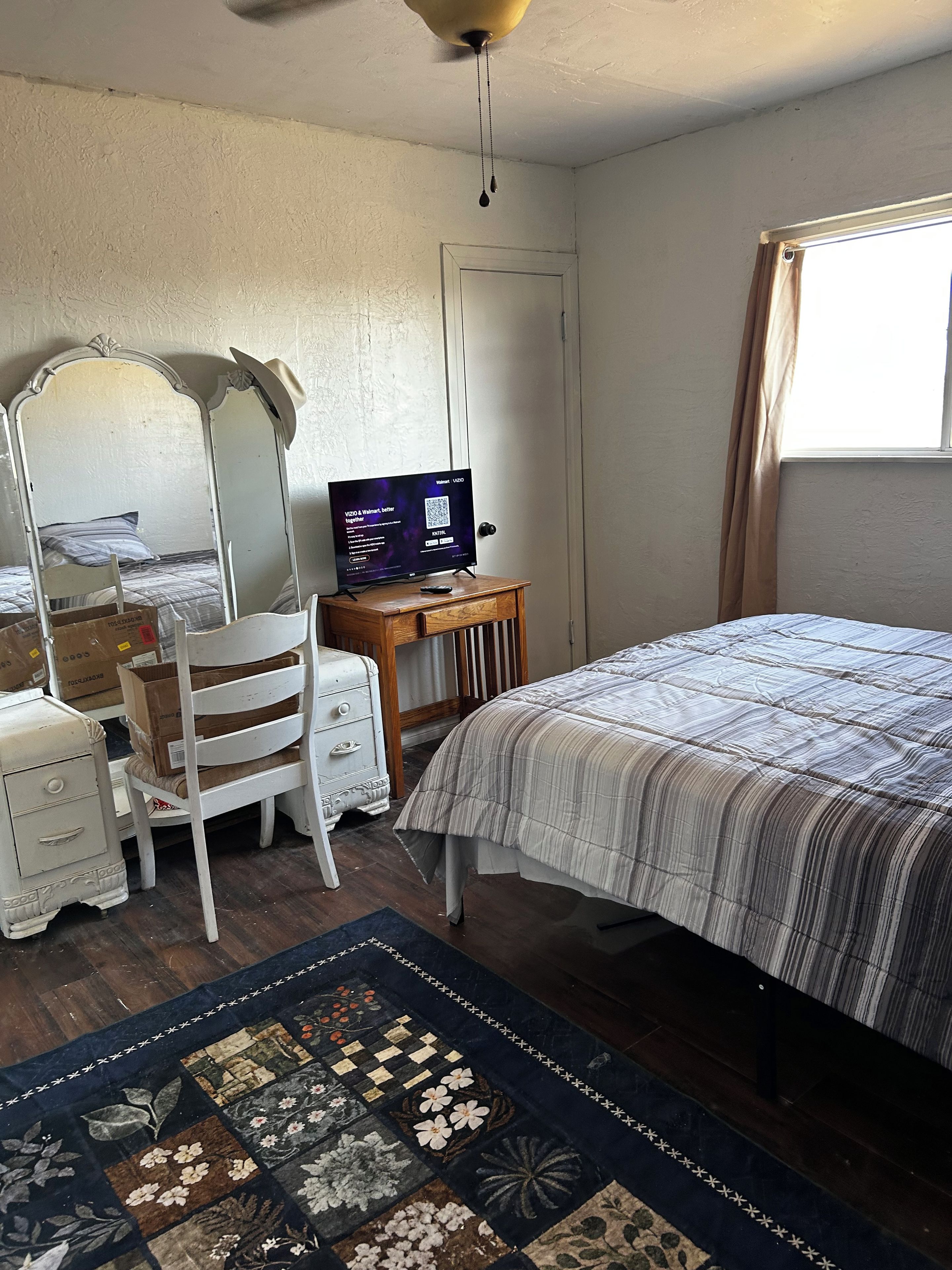 A bedroom with a bed, a desk with a computer, a chair, a dresser, and a window with curtains.
