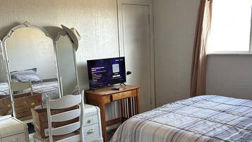 A bedroom with a bed, a desk with a computer, a chair, a dresser, and a window with curtains.