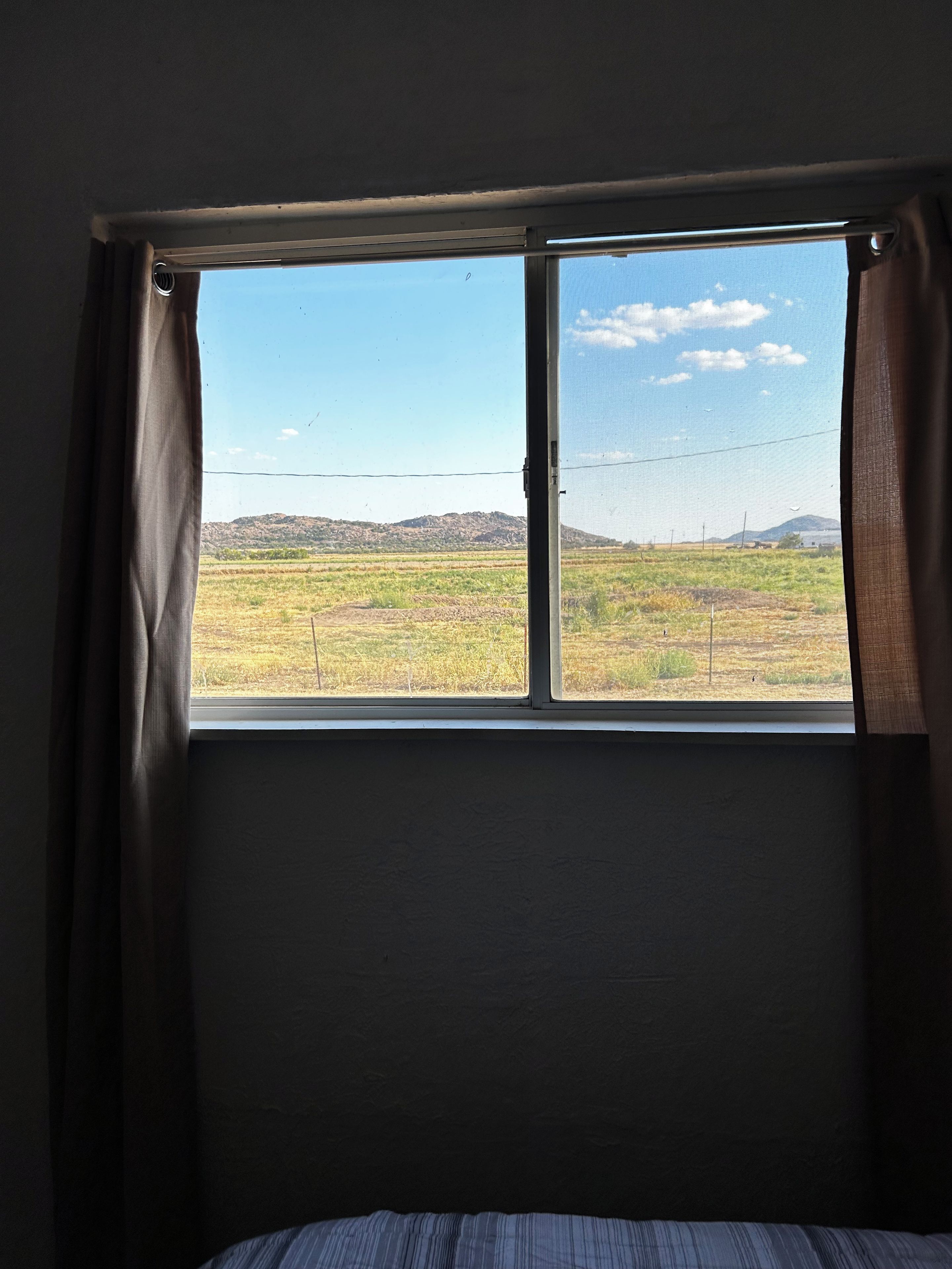 A room with a window overlooking a field and distant hills.