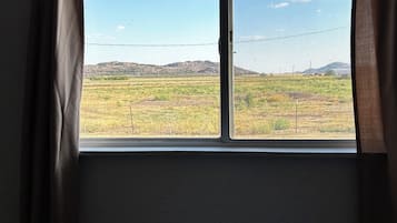 A room with a window overlooking a field and distant hills.